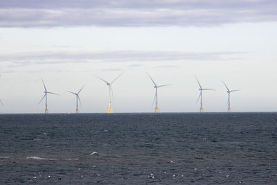 Wind turbines on land by sea against sky