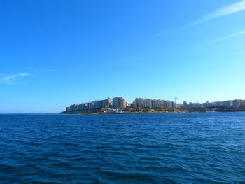 Sea by buildings against blue sky