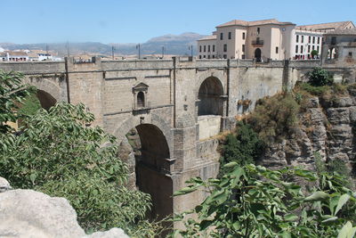 Arch bridge by buildings against sky