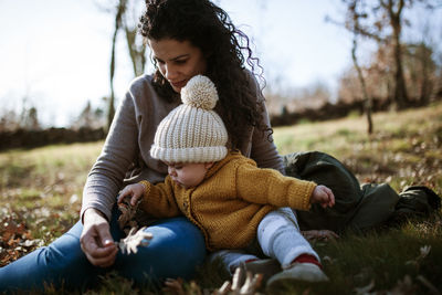 Mother and daughter wearing warm clothing while sitting on land