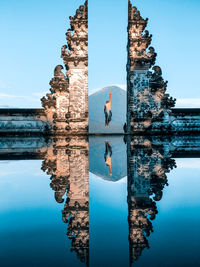 Rear view of man jumping with reflection in water at bali gate