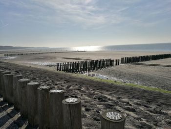 Wooden posts on beach by sea against sky