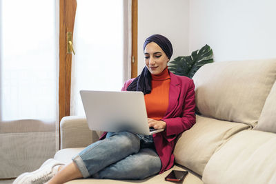 Young woman using laptop while sitting on sofa at home