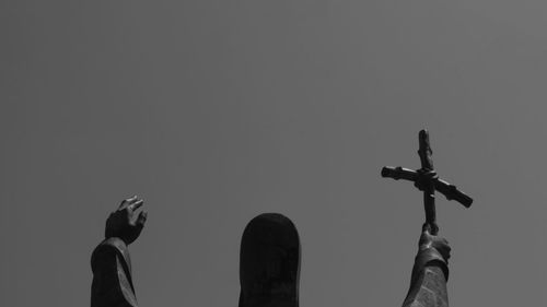 Low angle view of hand holding cross against sky