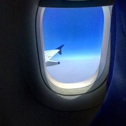 Close-up of airplane wing against sky seen through window