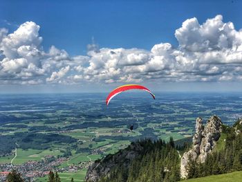 Silhouette person paragliding over landscape against sky