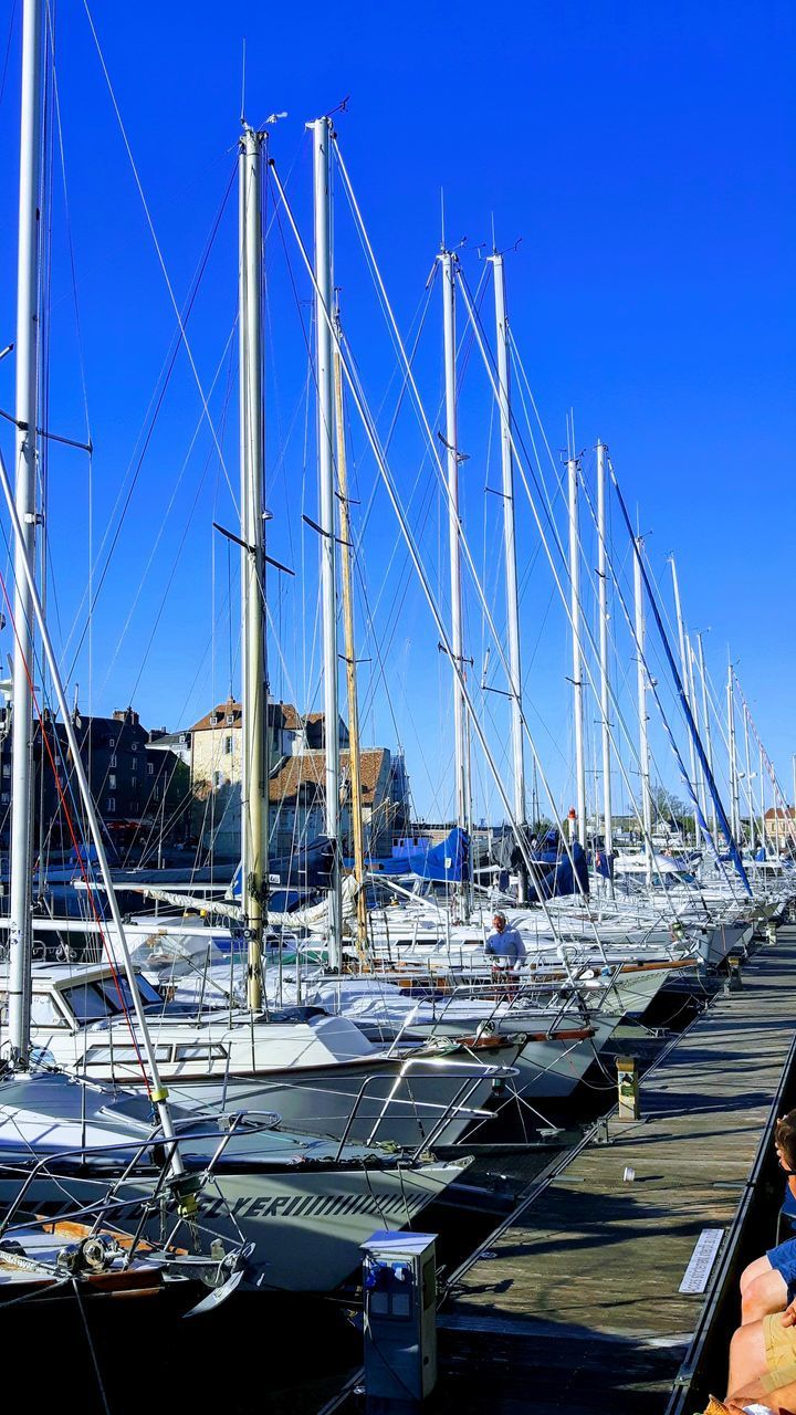 SAILBOATS MOORED AT HARBOR AGAINST BLUE SKY