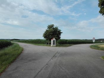 Empty road by trees against sky