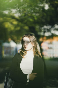 Thoughtful young woman standing against trees in city