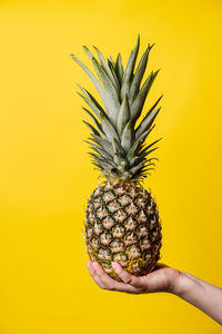 Close-up of hand holding fruit against yellow background