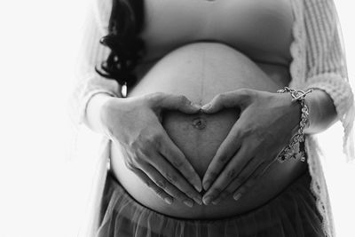 Midsection of pregnant woman making heart shape on stomach