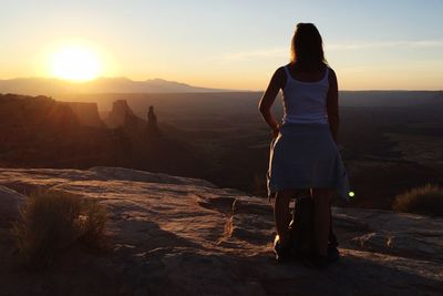 Rear view of woman standing on rock at sunset