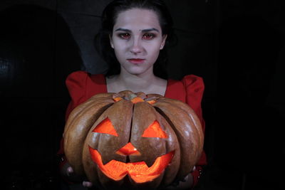 Portrait of woman holding pumpkin against black background