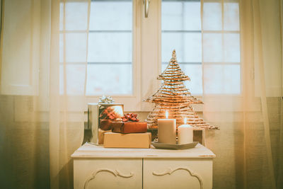 Gift boxes near lighted candles and christmas tree inside home. box with holiday ribbon with bows 