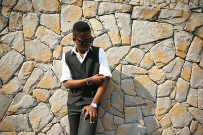 Boy wearing wearing sunglasses standing by stone wall