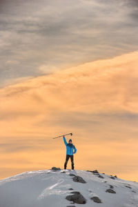 Man climbing on snowcapped mountain against cloudy sky during sunset