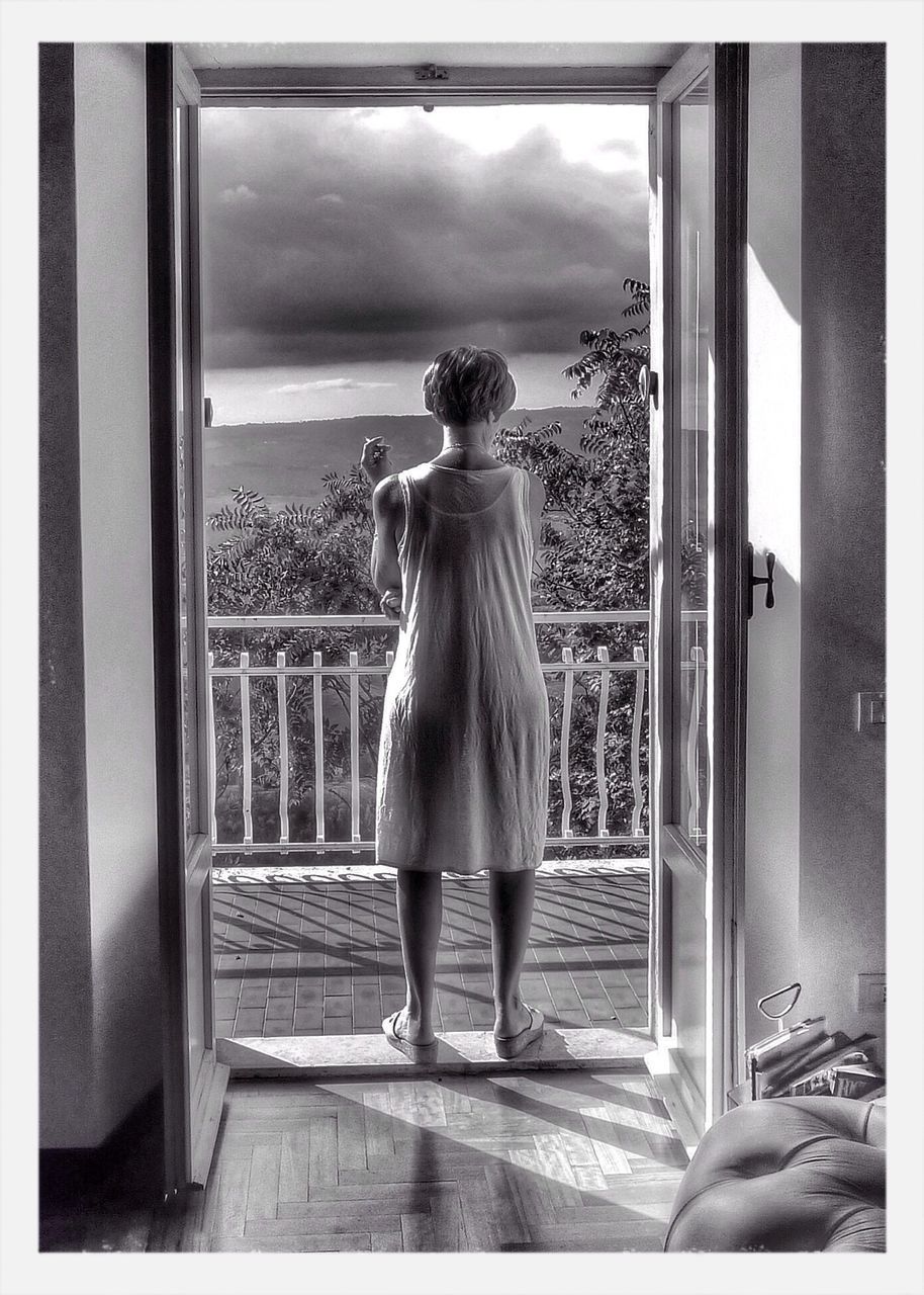 REAR VIEW OF WOMAN STANDING BY WINDOW IN BEDROOM