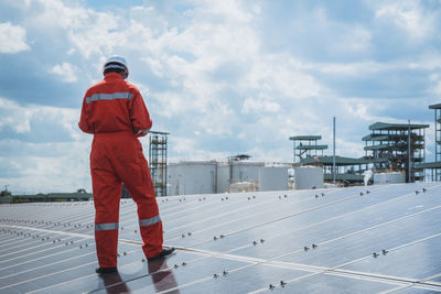 Engineer standing on solar panel against cloudy sky