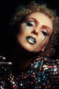 Portrait of a young woman with colorful and shiny makeup in the studio near black background