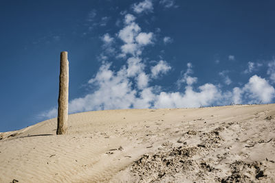 Low angle view of wooden pole on sand dune at beach against sky