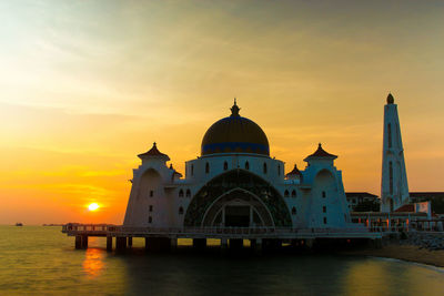 Malacca straits mosque by sea against sky during sunset