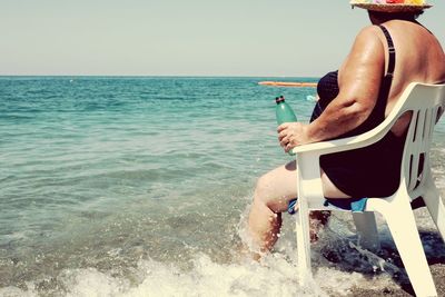 Rear view of man sitting on chair at beach