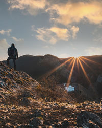 Rear view of man standing on mountain against sky during sunset