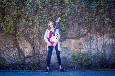 Full length of young woman with guitar standing against wall