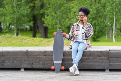 Happy african american woman skateboarder talk over phone call conversation outdoors in urban park