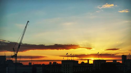 Low angle view of silhouette cranes against orange sky