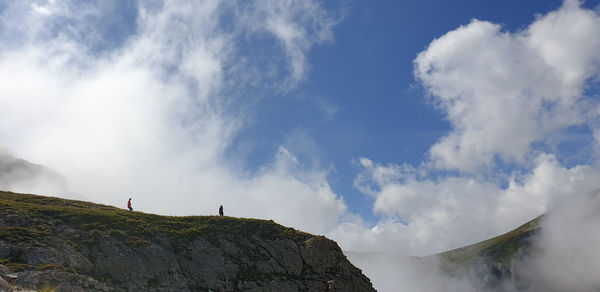Low angle view of people standing on rock against sky