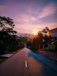 Street amidst trees and buildings against sky during sunset