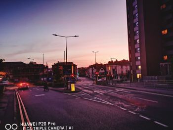 Illuminated city street against sky at sunset