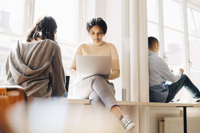 Computer programmers working on laptop by window in office