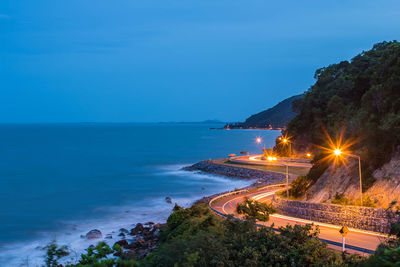 Scenic view of sea by light trails on road against blue sky at dusk