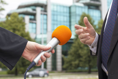 Cropped hand of female journalist with microphone taking interview of male politician