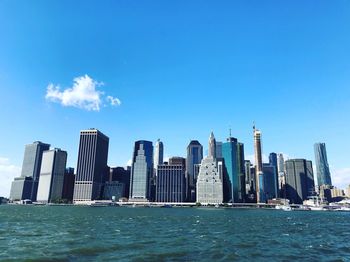 Sea by modern buildings against blue sky