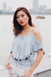 Portrait of young woman standing against river in city