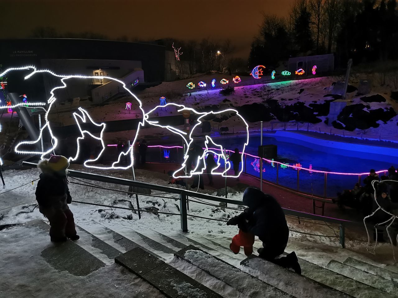 PEOPLE STANDING BY ILLUMINATED STREET AT NIGHT