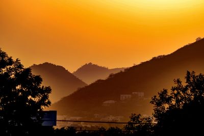 Silhouette of tree by mountain against orange sky