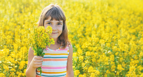 Portrait of cute girl holding flowers while standing in field