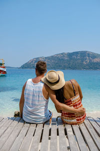 Rear view of man sitting on beach against clear sky