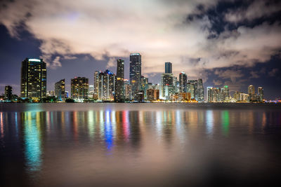 Illuminated city by buildings against sky at night