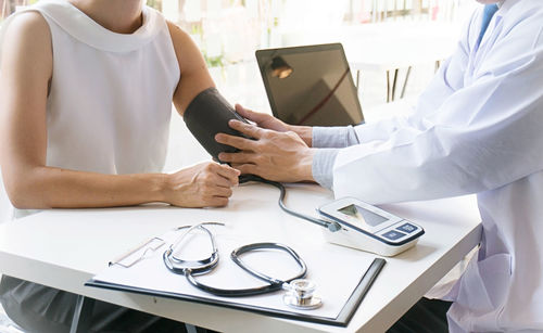 Cropped image of doctor checking blood pressure of patient at desk