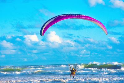 Person paragliding over sea against sky