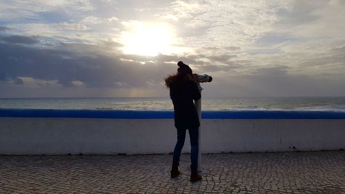 Full length of man photographing sea against sky during sunset