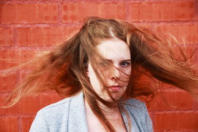 Close-up portrait of woman tossing hair while standing against wall