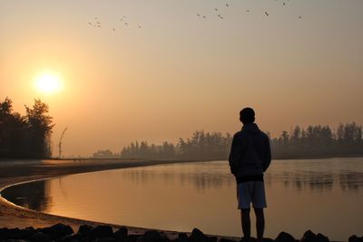 Man looking at lake against sky during sunset