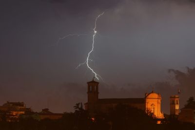 Lightning over illuminated buildings against sky at night