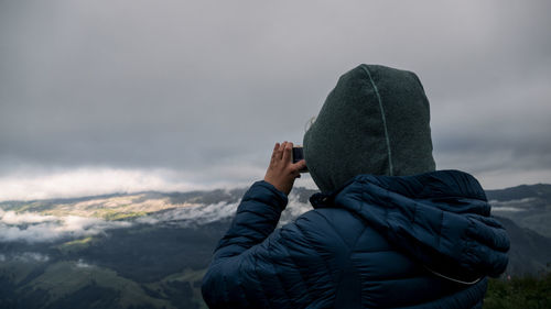 Rear view of woman photographing while standing on mountain against cloudy sky